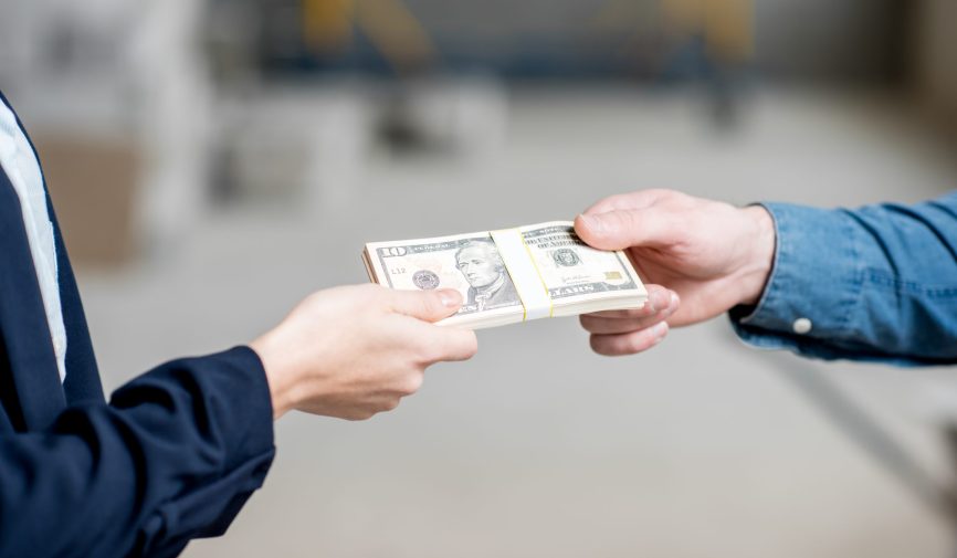 Businesswoman giving a money to builder for the work at the construction site. Close-up view focused on the hands