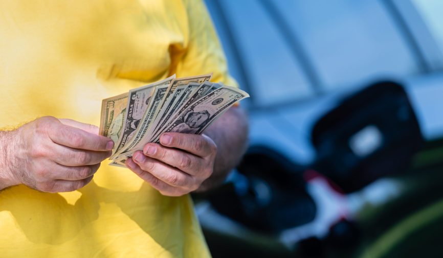 man holding dollar bills on background of car with open gas tank, close-up of hands